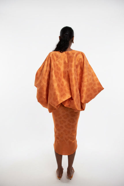 Person wearing an orange patterned outfit standing against a plain wall.