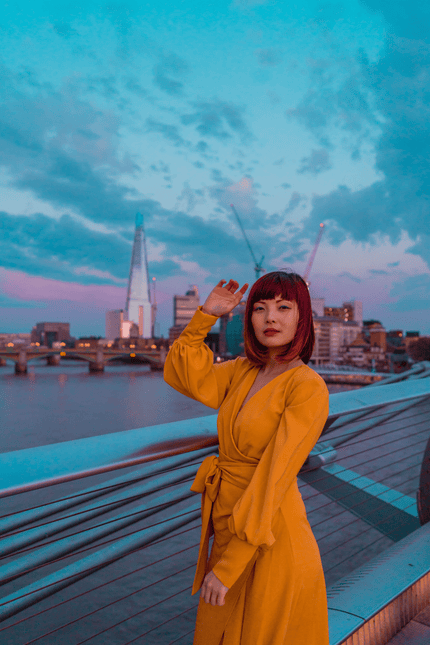Wearing the Sarvin Mustard Wrap Maxi Dress with balloon bishop sleeves, a person stands on a bridge at sunset, city skyline and the Shard visible in the background under a cloudy sky.