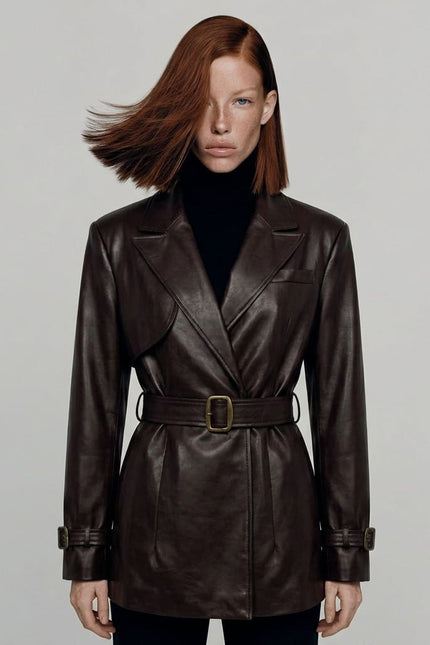 Woman wearing a brown leather coat with a belt on a plain background