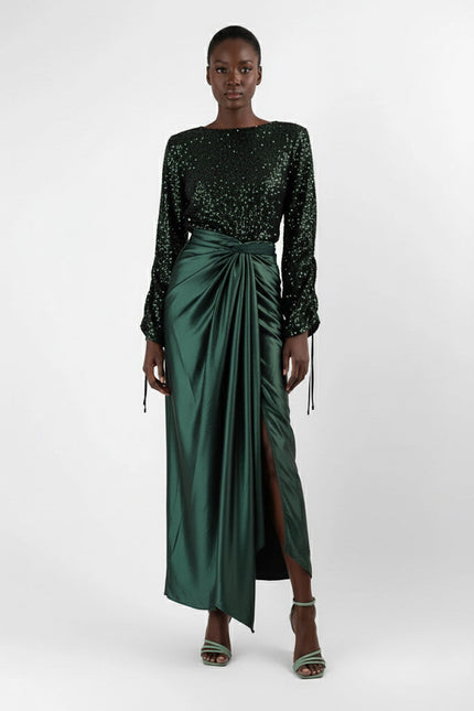 Woman wearing a black sequin top and green satin skirt on a white background