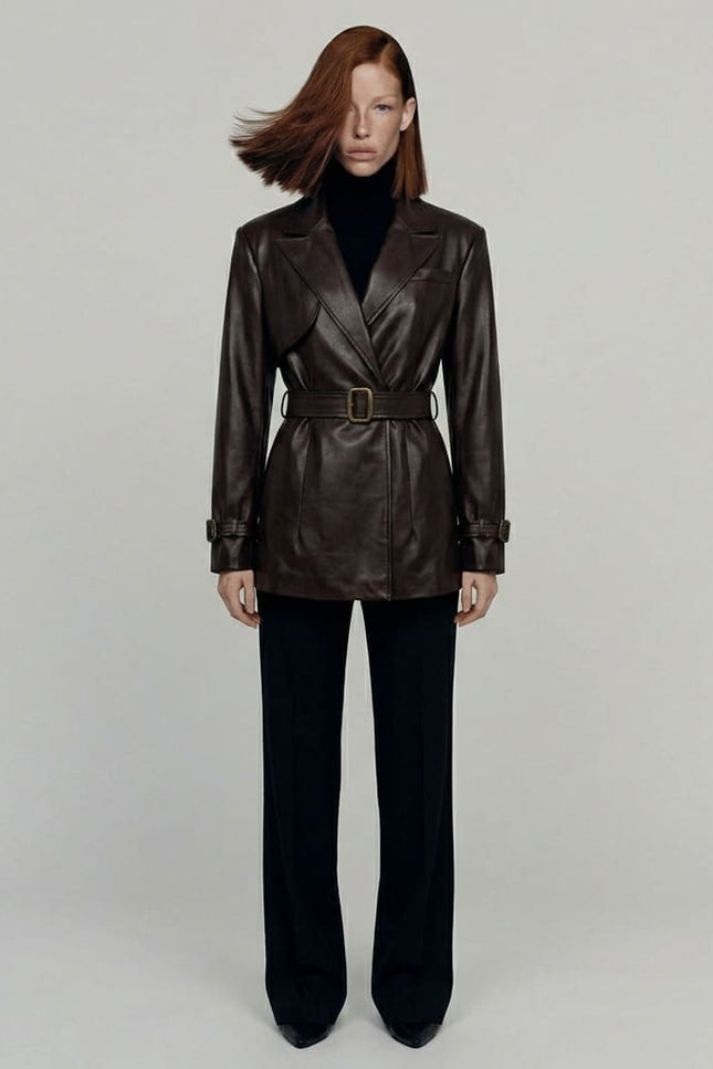 Woman wearing a brown leather trench coat and black pants on a plain background