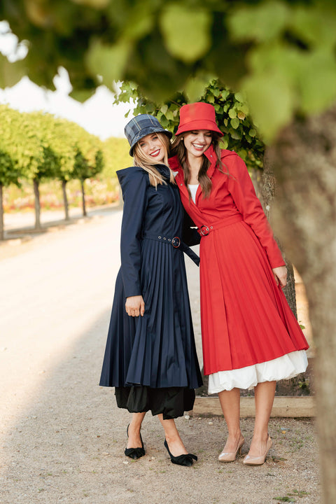 Two women in long coats standing outdoors with trees in the background