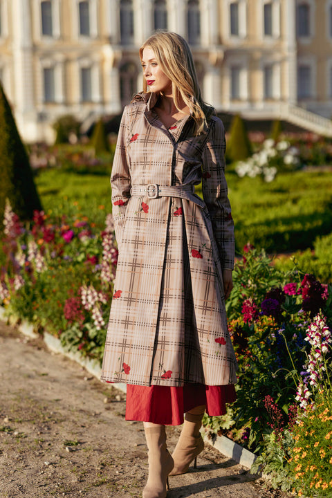Woman in a plaid coat standing in a garden with flowers and a building in the background