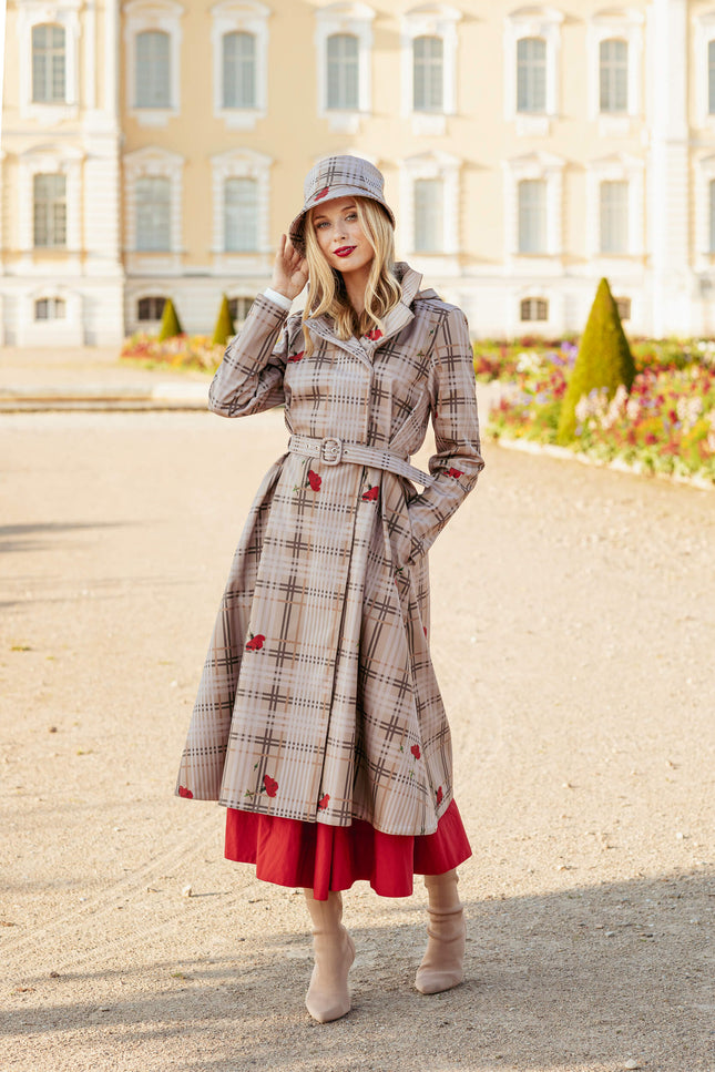Woman wearing a plaid coat with red accents and a matching hat, standing in front of a building.