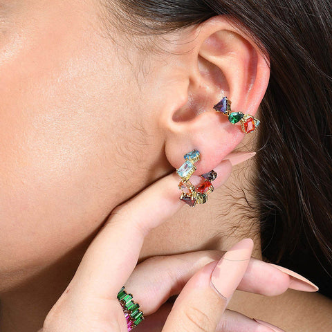 A person wearing a colorful ear cuff with a sculptural design, featuring multiple droplet shapes adorned with rich hand-applied enamel.