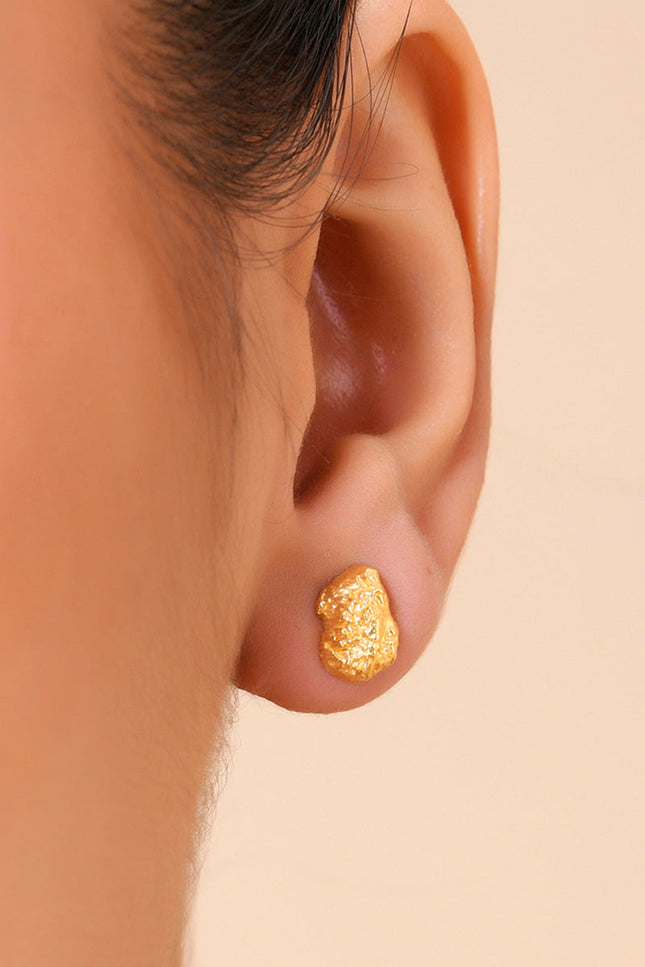 A close-up image of a person's ear wearing a gold-plated cobblestone textured stud earring.