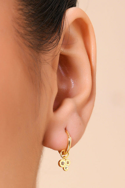 A close-up image of a person's ear wearing a gold-colored hoop earring with dangling crystals.