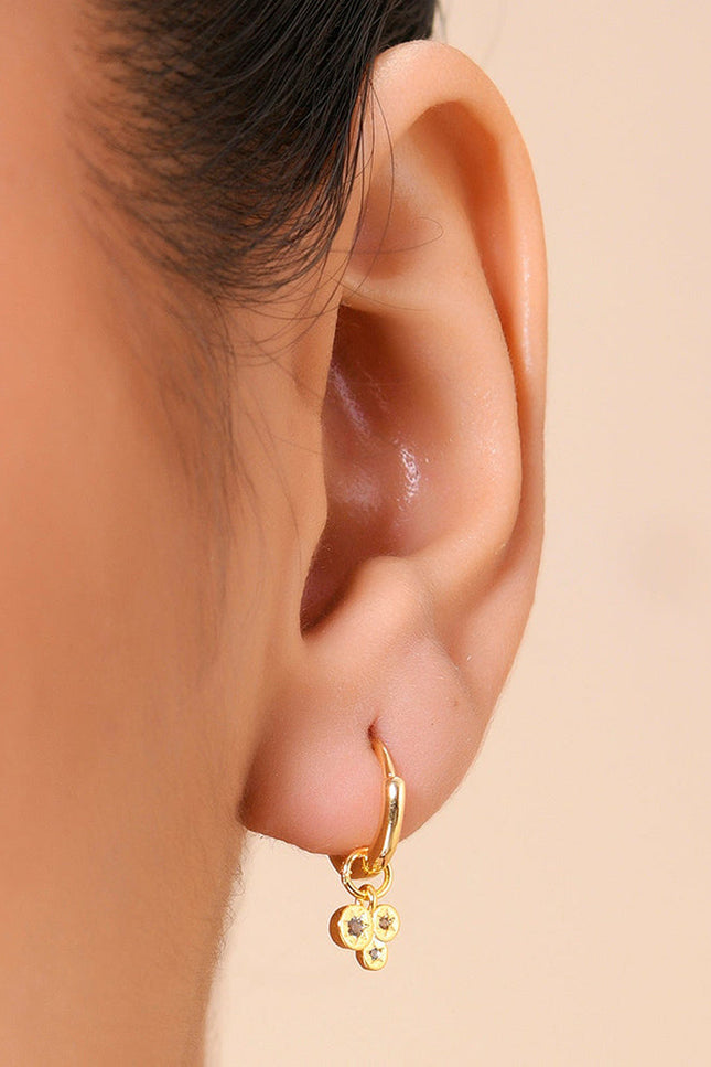 A close-up image of a person's ear wearing a gold-colored hoop earring with dangling crystals.