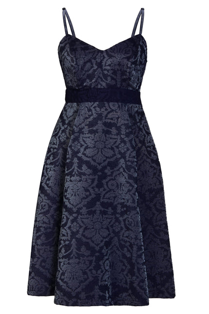 The Sarvin Jacquard Skater Dress is a sleeveless navy dress with thin straps, fitted bodice, A-line skirt, textured floral jacquard fabric, and an elegant velvet waistband accent.