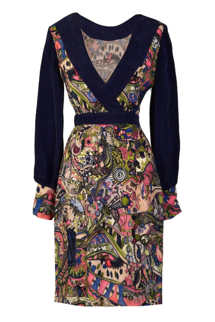 The Sarvin Hand Painted Long Sleeve Mini Dress features a deep V-neck, fitted waist, and solid dark blue upper bodice with sleeves. Colorful, intricate patterns adorn the skirt and sleeve cuffs for a striking Persian-inspired look.