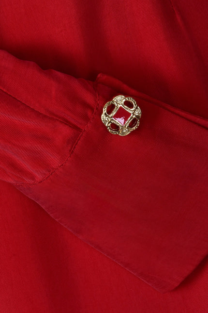 Close-up of the Long Sleeve Red Midi Dress by Sarvin, highlighting its red fabric sleeve and a decorative gold button with an ornate, textured design on the cuff.