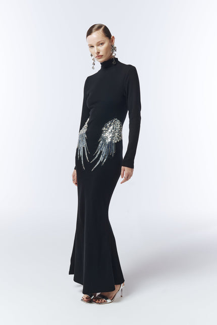 Model wearing long sleeve black evening gown with silver sequin wing details at hips.