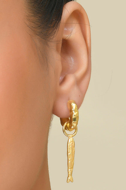 A person wearing a gold-Plated earring featuring a fish dangling over textured huggies.
