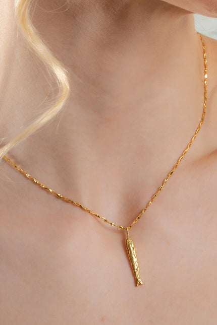 A close-up image of a person wearing a gold-colored necklace with a pendant shaped like a fish.