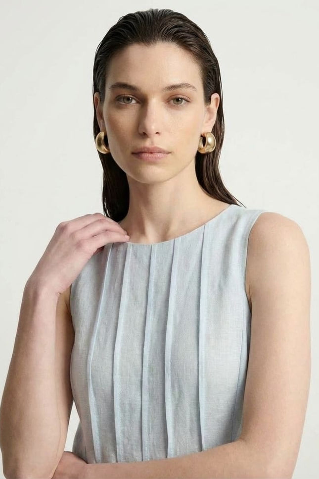 Woman wearing a light blue sleeveless dress against a plain background