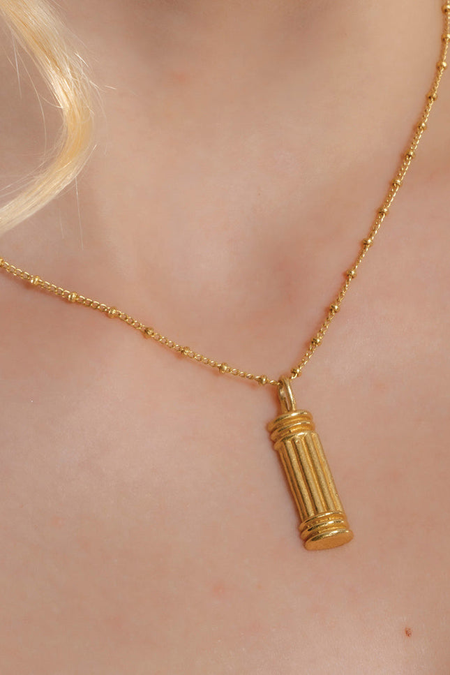 A gold-colored pillar-shaped necklace on a person's neck, showcasing a small, ornate charm.