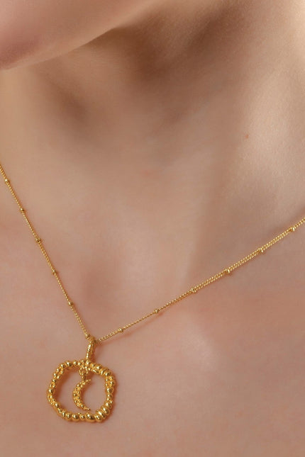 A person wearing a gold-colored necklace with a granulated texture circle pendant. Crescent moon necklace by Arvino