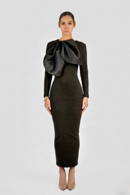 Black long-sleeve structured column maxi dress with oversized sculptural satin bow detail at chest, by Anitabel, styled with nude pointed heels