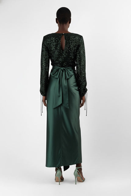 Woman wearing a black sequin top and green satin skirt on a white background