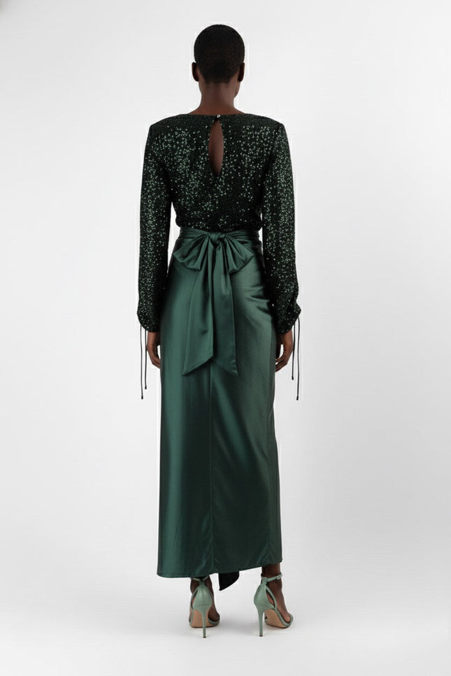 Woman wearing a black sequin top and green satin skirt on a white background