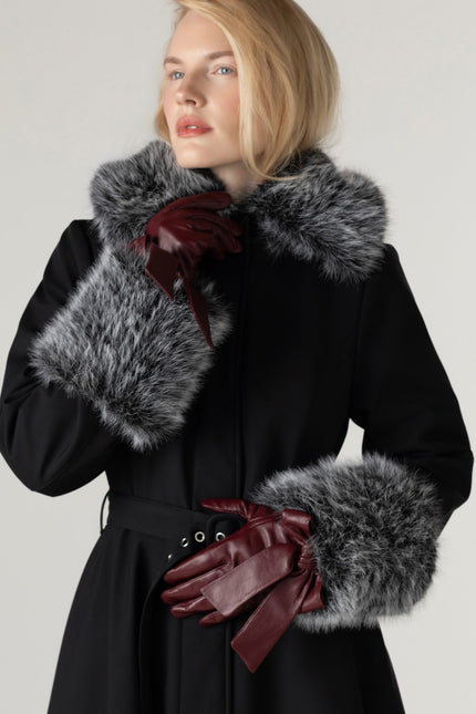 Close-up of the collar with the hood down on a women's black winter coat, highlighting the detachable faux fur collar and elegant tailored design leather gloves.