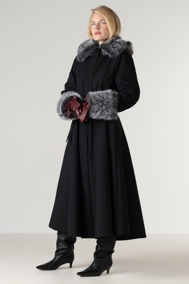 Full-length view of a women's black winter coat with removable faux fur, featuring a fitted bodice, flowing skirt, black Italian satin lining, and a matching buckle belt.