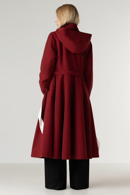 Back view of a women's deep red winter coat highlighting the elegant fit and flare silhouette, flowing skirt, and removable hood.