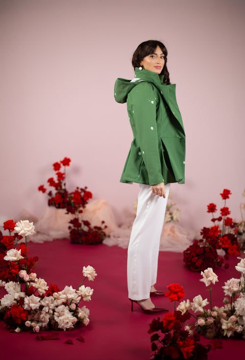 Woman in a green coat standing in front of floral decorations on a pink background
