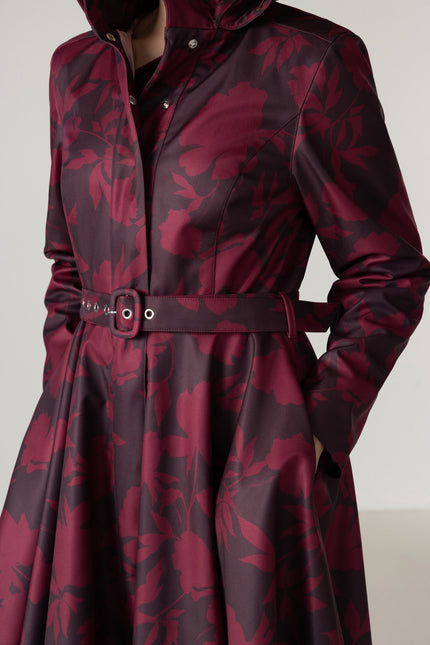 A close-up of a long-sleeve hooded coat with a dark floral pattern in deep burgundy and dark brown, featuring a matching belt with silver-tone buckle details.
