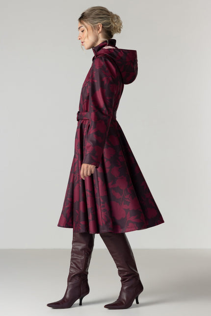 A woman in profile wearing a long hooded coat with a dark red and black floral pattern by RainSisters.