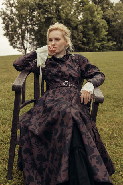 Model sitting outdoors wearing the Women's Brown Floral Fit and Flare Coat Brocade Dusk, showcasing the waterproof softshell fabric, elegant floral print, and timeless feminine silhouette.