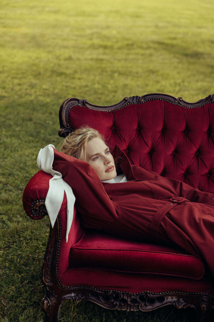 Model sitting outdoors wearing a women's deep red fit and flare winter coat in a rich maroon shade with a timeless feminine silhouette.