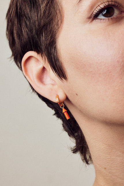  image of rocket enamel earrings in orange and gold shown close-up of ear and eye on model with white skin and short brown hair