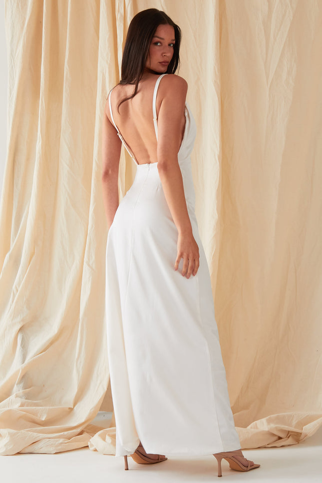 A person with long dark hair wears the Sarvin Ivory Satin Asymmetric Backless Maxi Dress, posing before beige fabric drapes in nude heeled sandals and looking over their shoulder in this elegant evening gown.