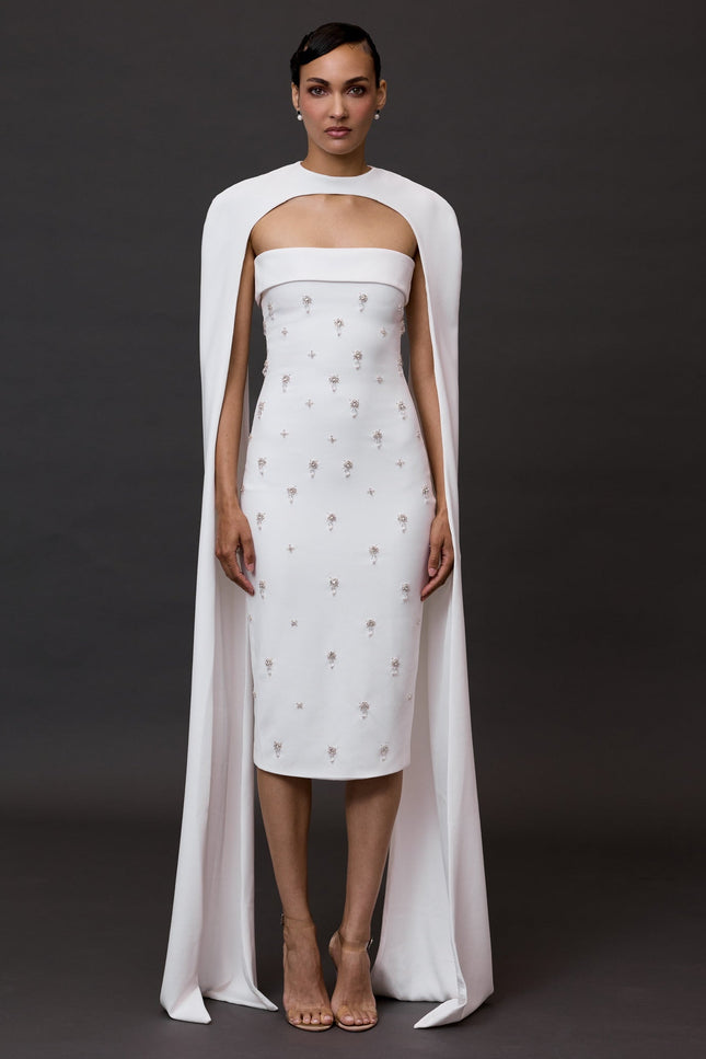 Model wearing a white dress with a long cape against a dark background