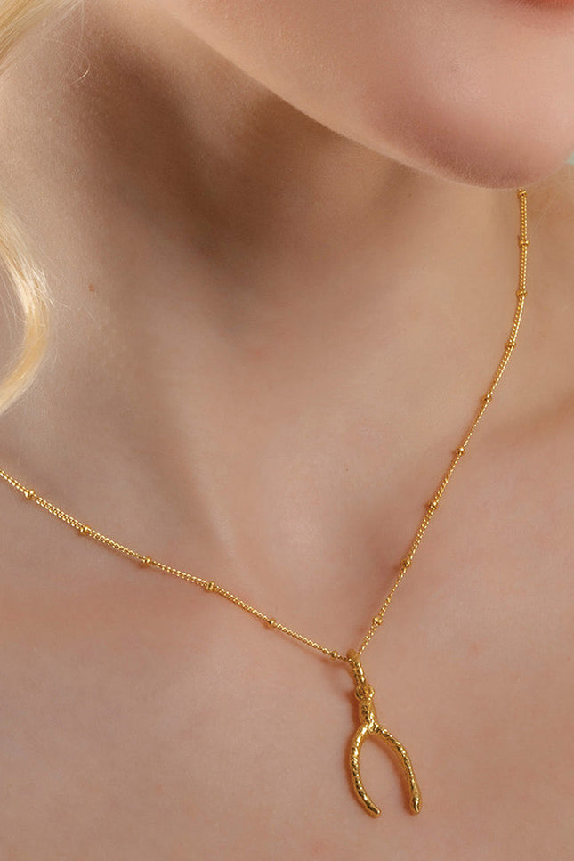 A person wearing a gold-colored necklace with a wishbone-shaped pendant By arvino