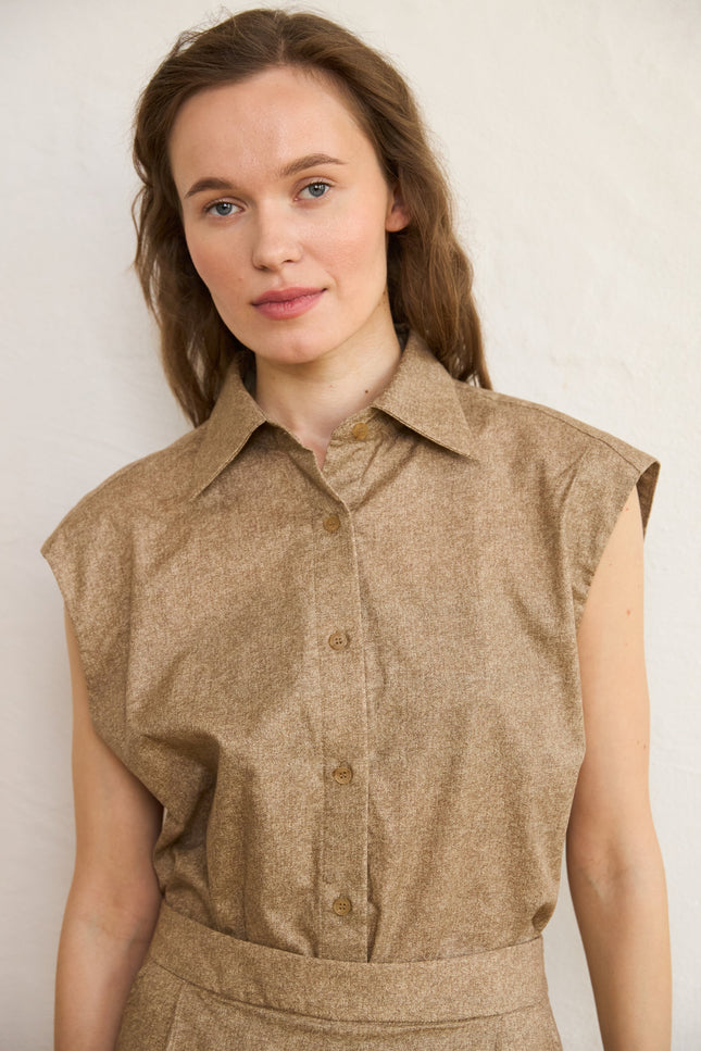 Woman wearing a brown sleeveless blouse against a plain background