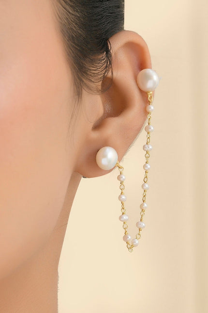 A person wearing a pearl earring with a delicate gold plated chain designed to wrap around the ear.