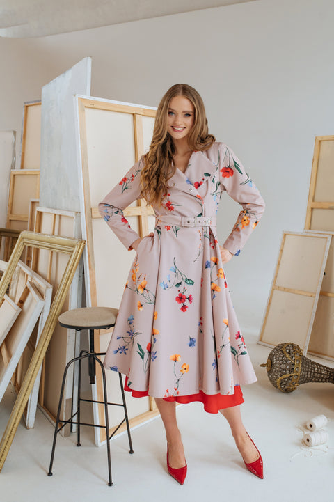 A woman standing in an art studio wearing a beige double-breasted trench coat with a colorful floral print.