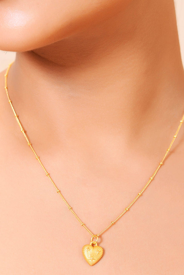 A gold-plated pendant necklace with a heart-shaped pendant and a chain, displayed on model neck