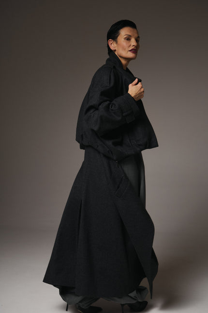 Person wearing a long black coat against a plain background