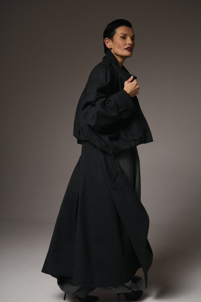 Person wearing a long black coat against a plain background
