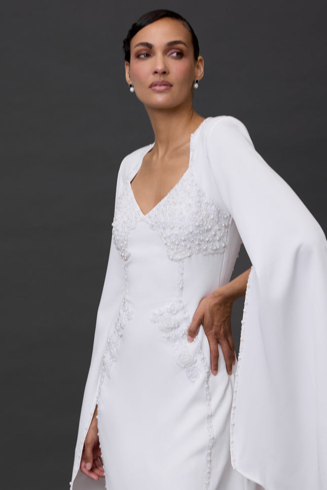 A woman modeling a white mini dress with long sleeves and a V-neckline, featuring a flowing skirt.