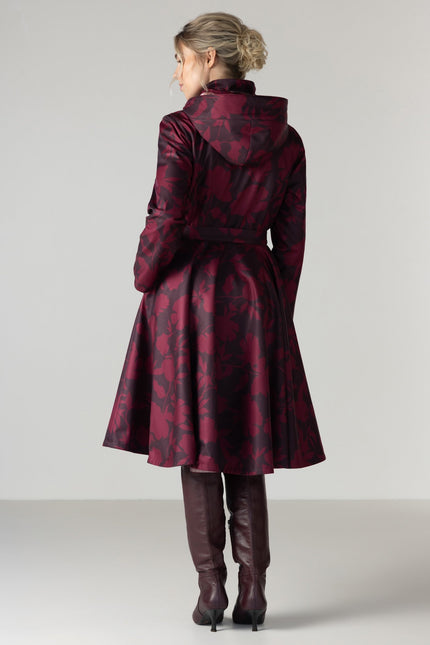 A woman viewed from the back wearing a dark red and black patterned hooded coat with a waist belt by RainSisters.