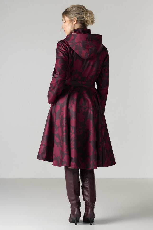 A woman viewed from the back wearing a dark red and black patterned hooded coat with a waist belt by RainSisters.