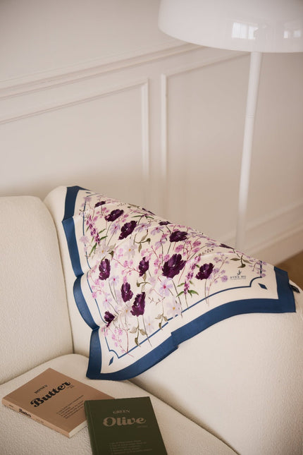 Angel Flower Blessing silk scarf draped elegantly over a white couch with books, showcasing the luxury pure silk accessory in a cozy home setting.