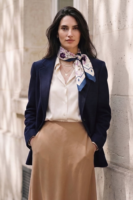 Model wearing NINA HO ILLUSTRATION Angel Flower Blessing silk scarf with a beige skirt and dark blazer in an urban street setting.