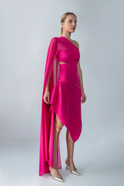 Woman wearing a vibrant pink one-shoulder dress with a cape on a white background