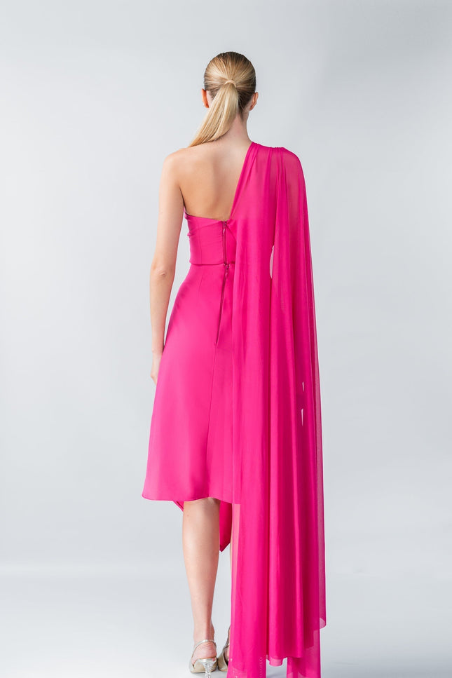 Woman wearing a vibrant pink one-shoulder dress with a cape on a white background