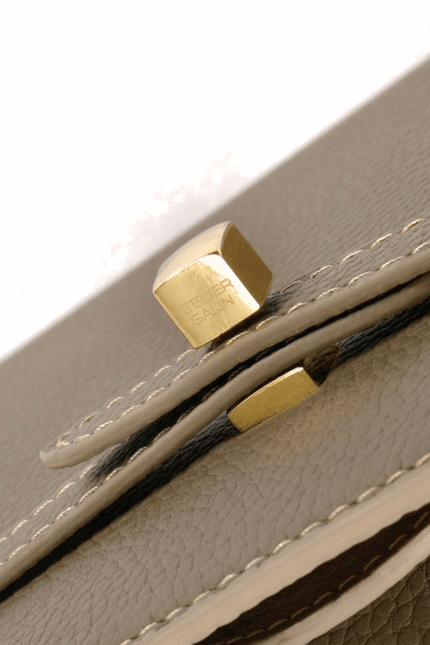 Close-up of a beige leather bag with gold atelier galin logo cube lock hardware on a white background